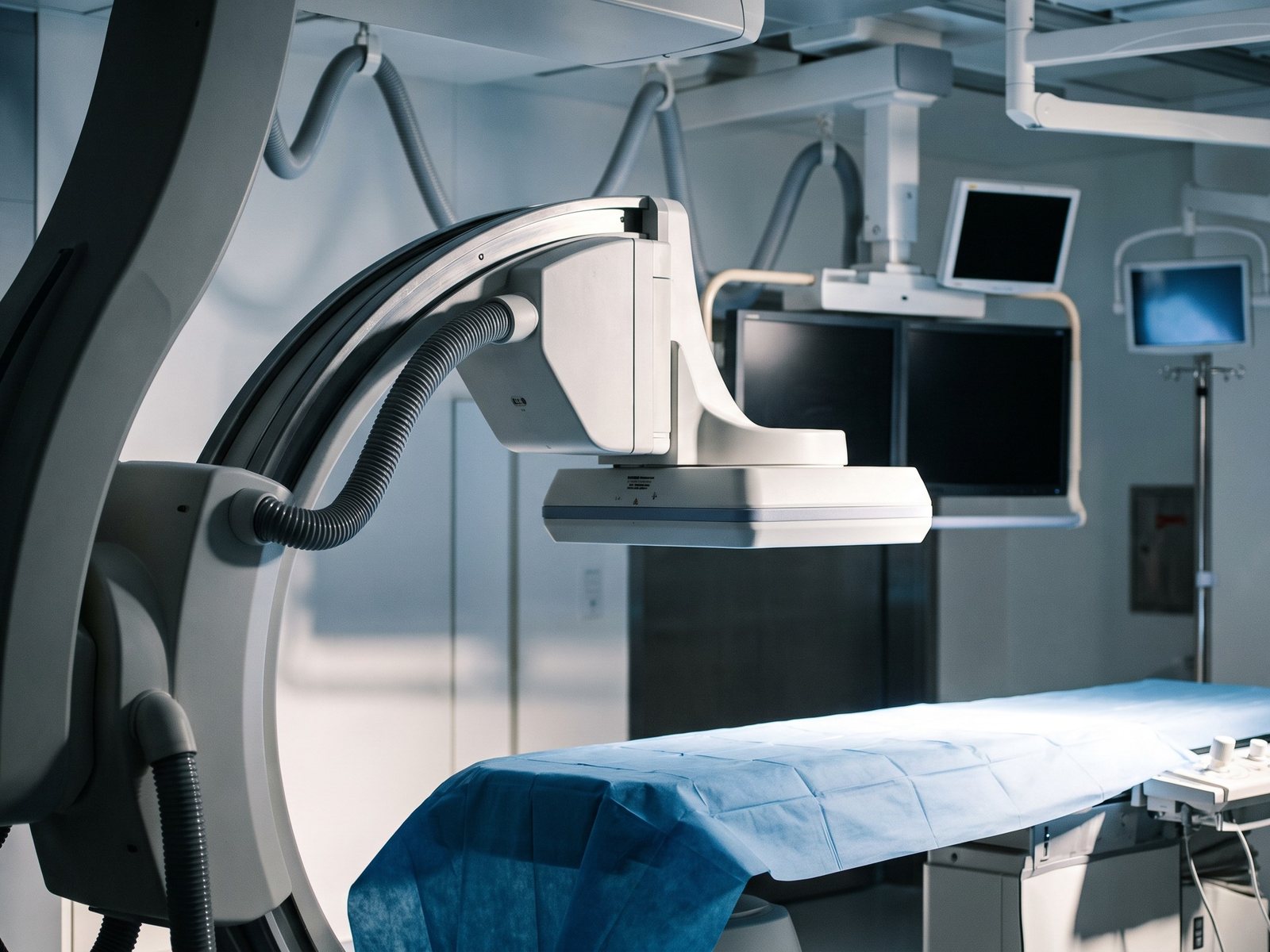 An empty cardiac catheter laboratory with the X-ray camera and procedure table (illustrative image)